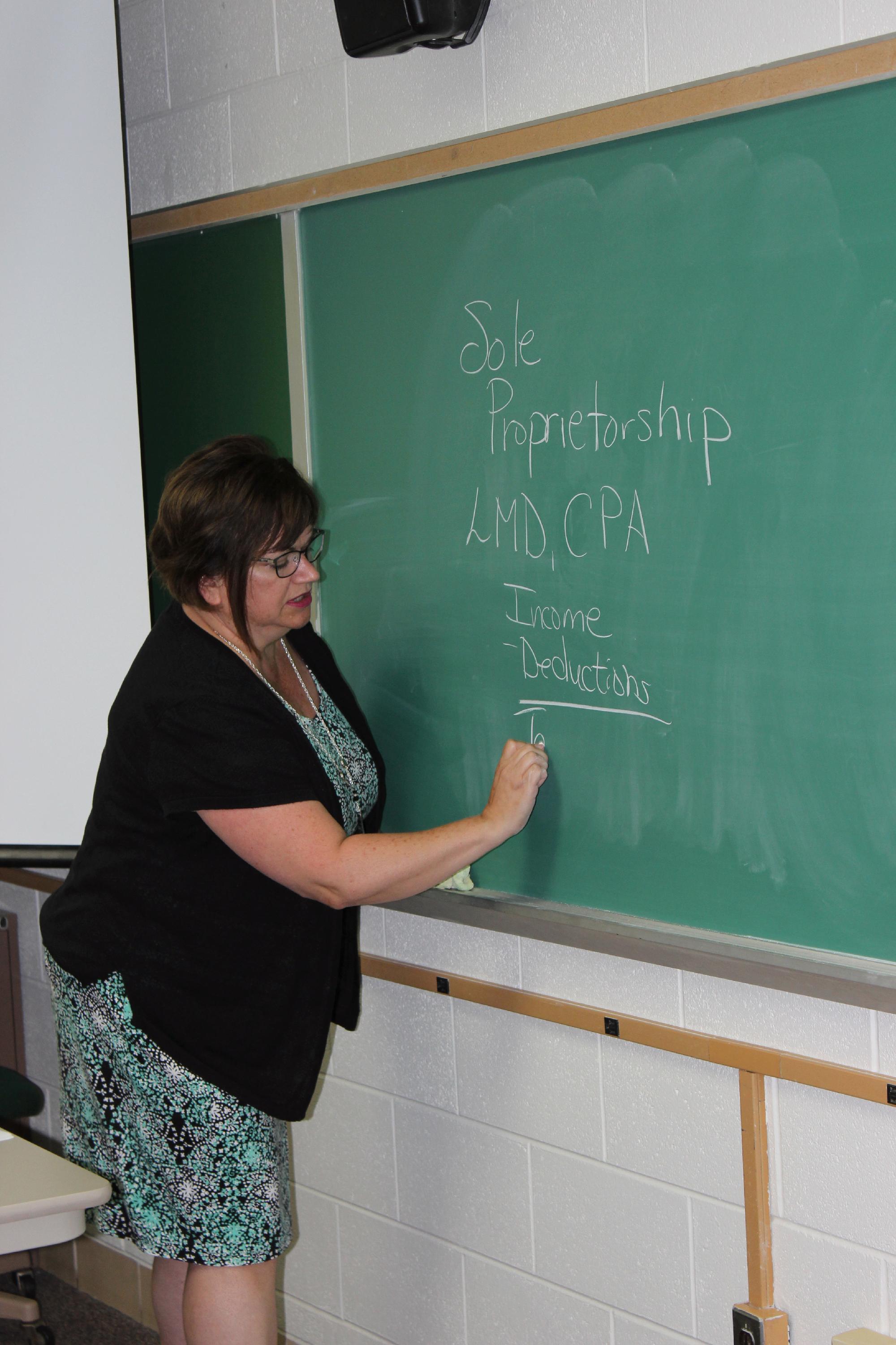 Accounting Faculty Lois Darga writes notes on the chalkboard